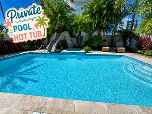 Une piscine privée avec un jacuzzi, entourée de palmiers et surplombant un ciel d’un bleu limpide.