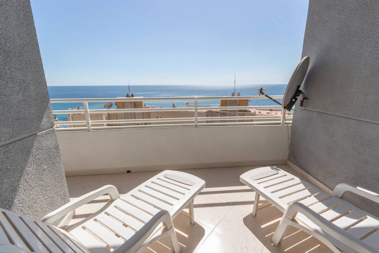 Un balcón con sillas de plástico blanco, una antena parabólica y vista al mar.