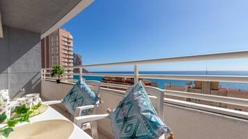 Een balkon met witte stoelen en een tafel, met uitzicht op een strand en de zee.
