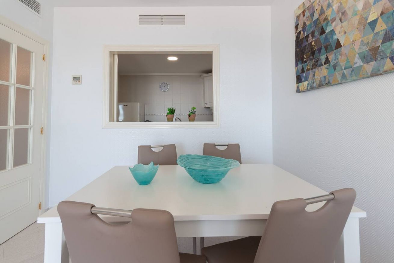 Un comedor con una mesa blanca, cuatro sillas y un espejo grande encima de la mesa.