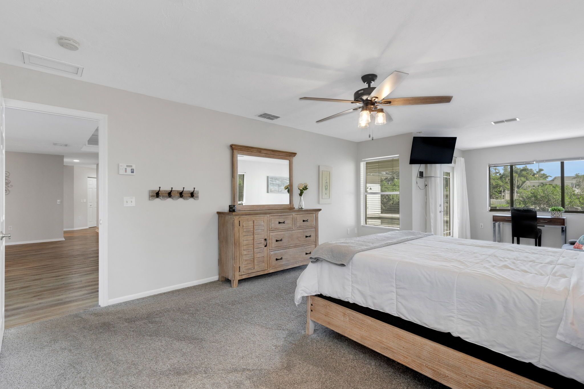 A bedroom with a large bed, a ceiling fan, a dresser, a mirror, and a TV.