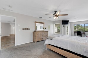 Ein Schlafzimmer mit einem großen Bett, einem Deckenventilator, einem Schminktisch, einem Spiegel und einem Fernseher.