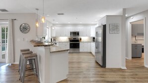 Eine moderne Küche mit weißen Schränken, Edelstahlgeräten und einer Holztheke mit Hockern.