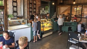Ein gemütliches Café mit Backsteinwänden, einer Theke mit einer Auslage und Gästen an Tischen.