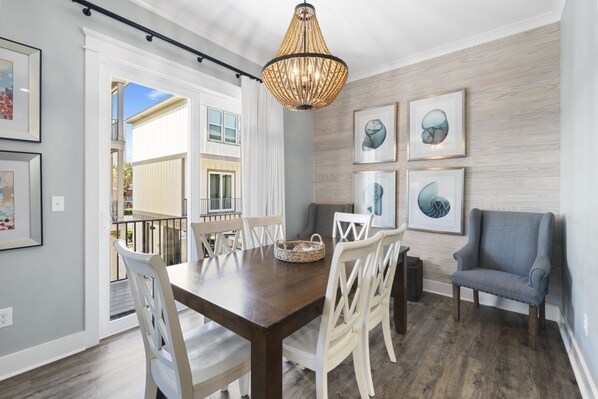 A dining area with a wooden table, white chairs, a blue armchair, and a woven light fixture.