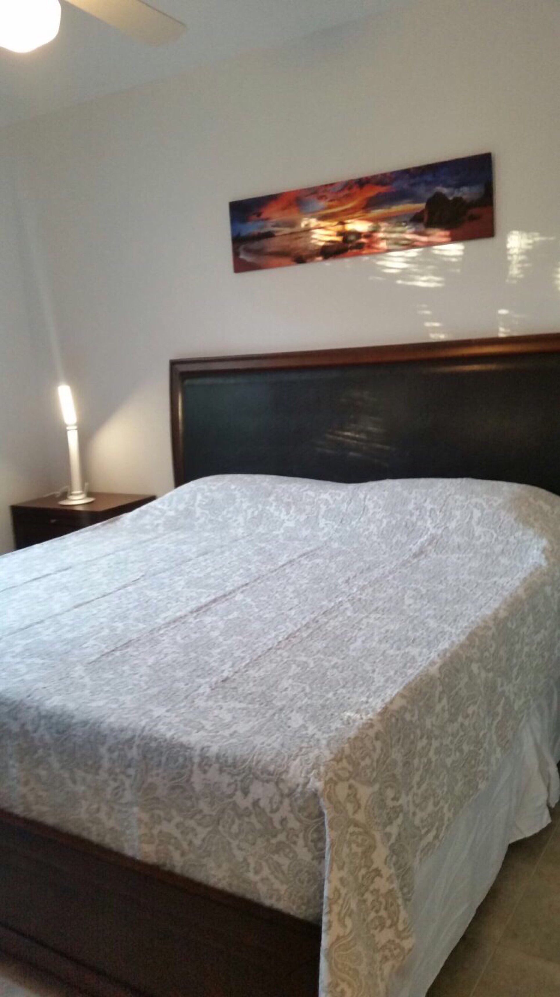 Ein Schlafzimmer mit einem Bett, einem Nachttisch, einer Lampe und einem Gemälde an der Wand.