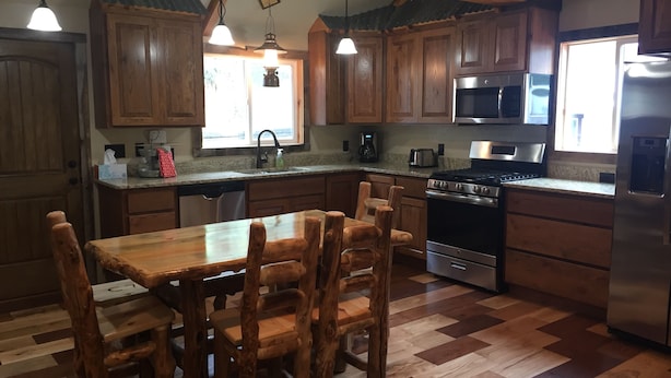 A kitchen with wooden cabinets, a dining table with chairs, a stove, a microwave, and a refrigerator.