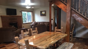 A rustic wooden dining table with benches, a fireplace, a sofa, and a staircase.