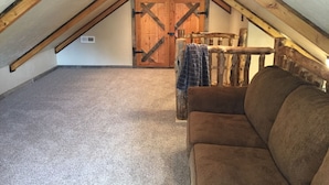 An attic room with a sloped ceiling, exposed wooden beams, a brown couch, and a rustic wooden door.