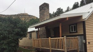 A two-story house with a stone chimney, a wooden porch, and a small garden area.