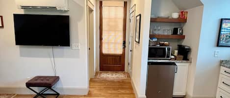 Una cocina moderna con microondas, tostadora y armarios. Se ve un refrigerador pequeño y un televisor montado en la pared.