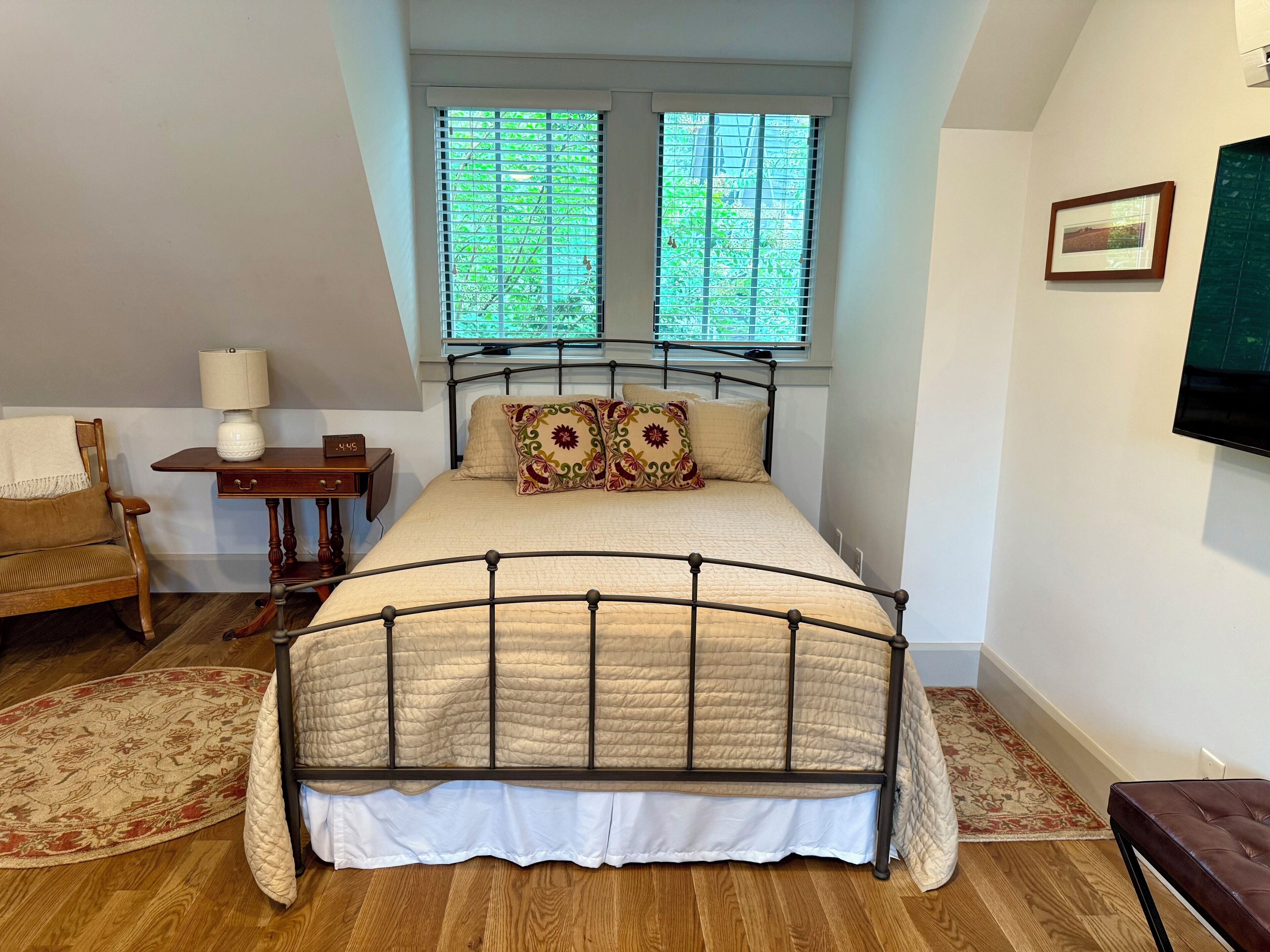 Une chambre à coucher comprenant un lit, une chaise, une table de chevet, une lampe et une fenêtre avec des stores.