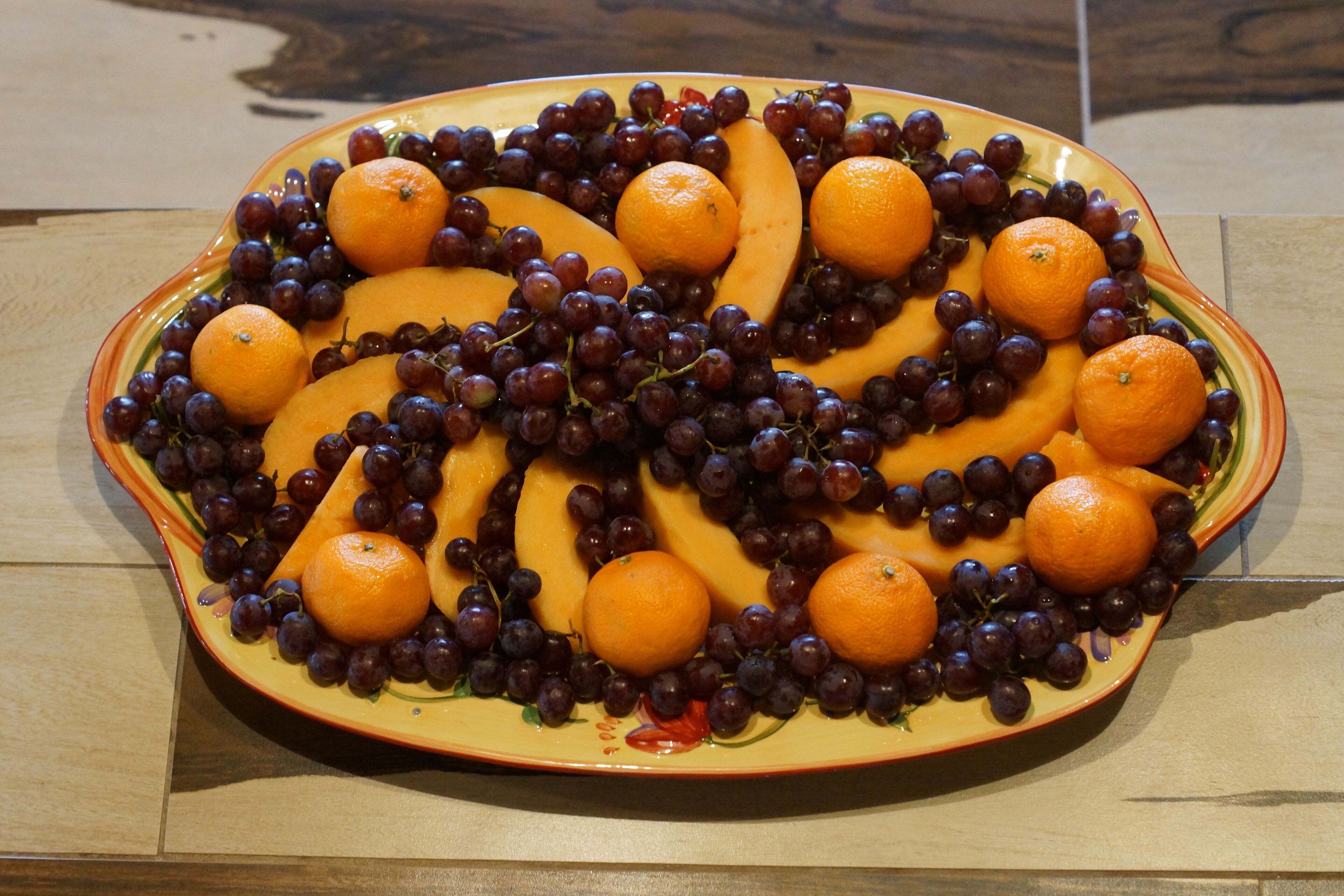 A fruit platter with oranges and grapes arranged on a ceramic plate.