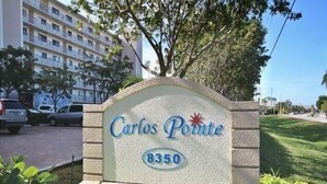 Un letrero que dice 'Carlos Pointe' con el número 8350, rodeado de follaje y un área de estacionamiento con coches.
