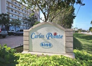 A sign for 'Carlos Pointe' with the number 8350, surrounded by greenery and a parking area with cars.