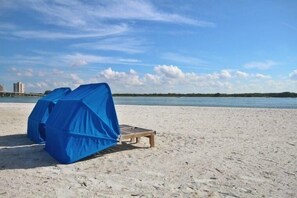 A beach with two covered lounge chairs and a wooden bench.
