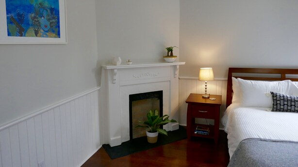 A hotel room with a white fireplace, a bed with white bedding, a nightstand with a lamp, and a framed painting on the wall. - Spacious home in the Historic District. Sleeps 8. Free Parking (Savannah)