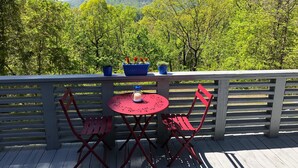 Una terraza de madera con una mesa y sillas, con vista a una cadena montañosa boscosa.