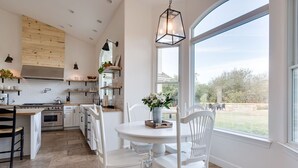 A modern kitchen with white cabinetry, a central island, and a large window offering a view of the outdoors. - Avila Valley Luxury Estate with Pickleball Court (San Luis Obispo)