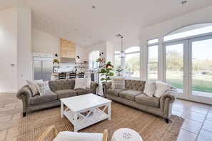 A spacious living area with a grey sectional sofa, a white coffee table, and a large window offering a view of the outdoors. - Avila Valley Luxury Estate with Pickleball Court (San Luis Obispo)