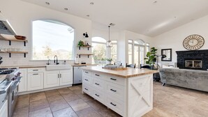 A modern kitchen with white cabinetry, a large island, and a fireplace. - Avila Valley Luxury Estate with Pickleball Court (San Luis Obispo)