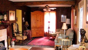 Un salon chaleureux avec une cheminée, un meuble en bois, un canapé, un fauteuil et une petite table agrémentée d’objets décoratifs.