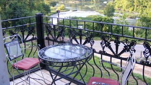 Un balcon avec une table et des chaises en verre, donnant sur une rivière et une zone boisée.