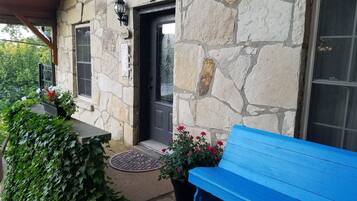 A stone building with a dark door, a blue bench, and potted plants with red flowers.