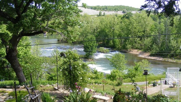 Un jardin au bord de la rivière, avec un banc, une mangeoire à oiseaux et une clôture blanche.