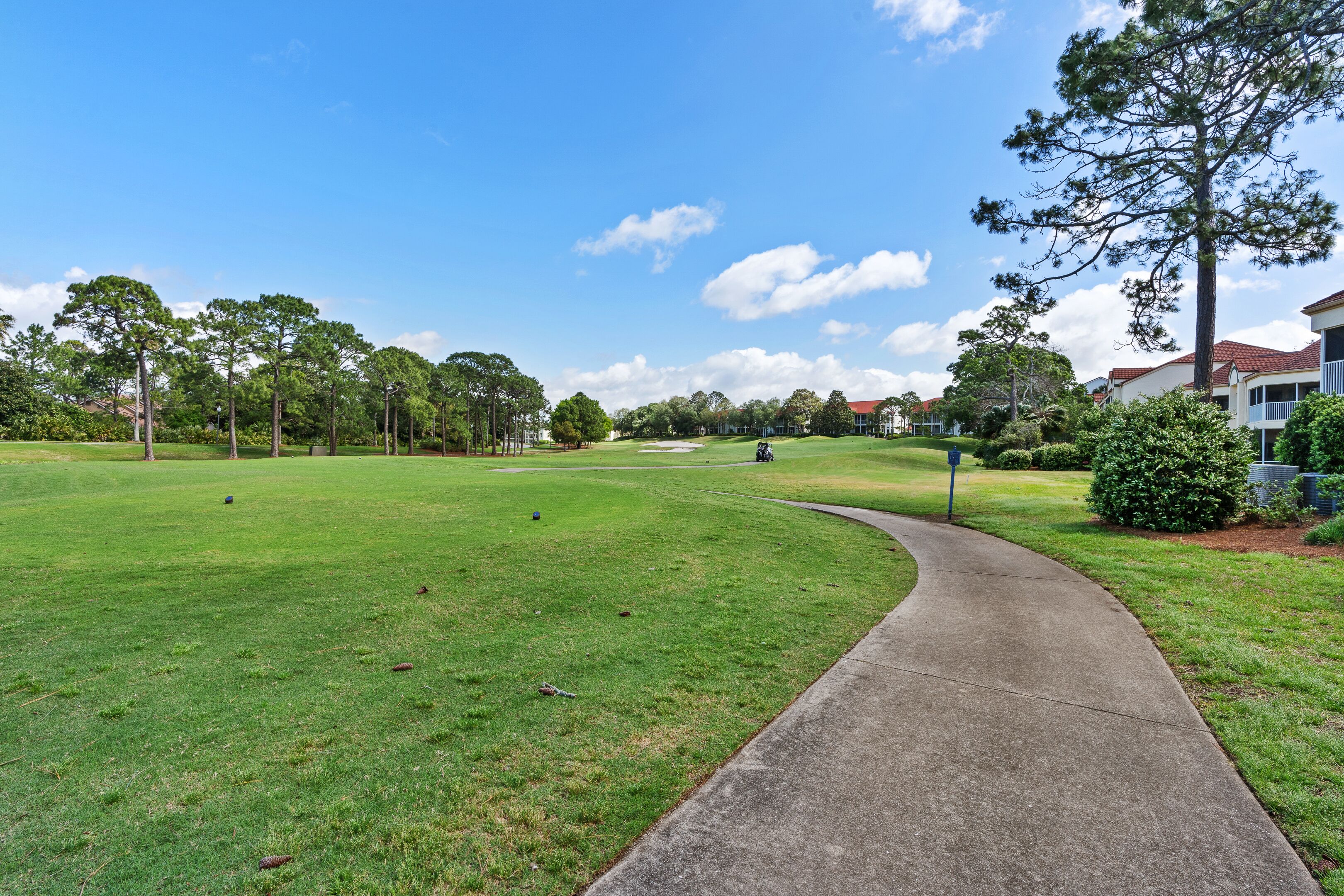 A golf course with a curved concrete path, surrounded by trees and residential buildings.