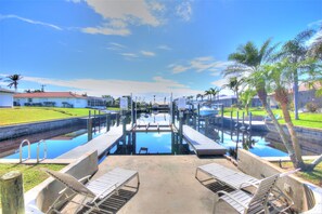 A swimming pool with a dock, lounge chairs, and a clear sky. - 5 bedroom, South facing, FREE heated salt water pool, with Direct Gulf access (Cape Coral)