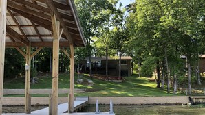 Une terrasse en bois avec un espace abrité, une pelouse et une maison en arrière-plan.