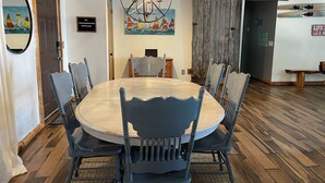 Un coin repas avec une table ronde et six chaises, un lustre et un tableau représentant des voiliers.