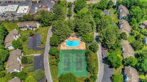 Luchtbeeld van een woongebied met een tennisbaan, omgeven door huizen en begroeiing.