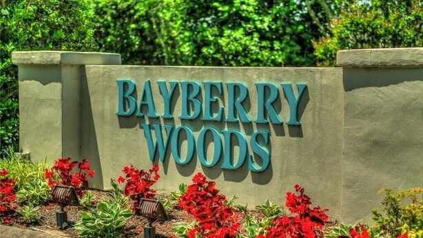 Een bordje voor Bayberry Woods, met een stenen muur en rode bloemen ervoor.