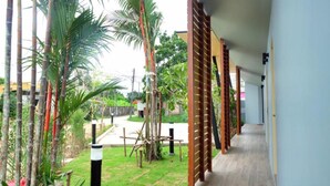 A corridor with a wooden floor, bamboo plants, and a view of a road and greenery outside. - Phumi Resort (Thep Krasattri)