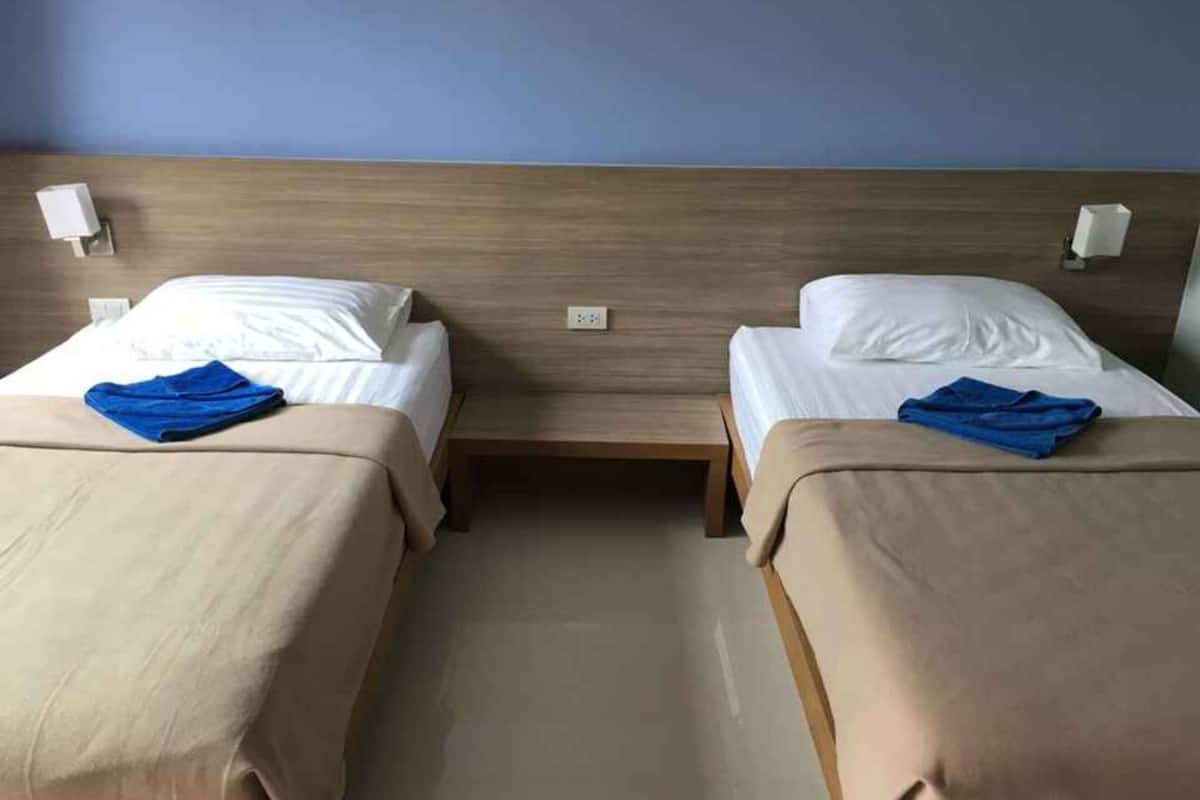 A hotel room with two single beds, each with a blue towel, wooden headboard, and bedside lamps.
