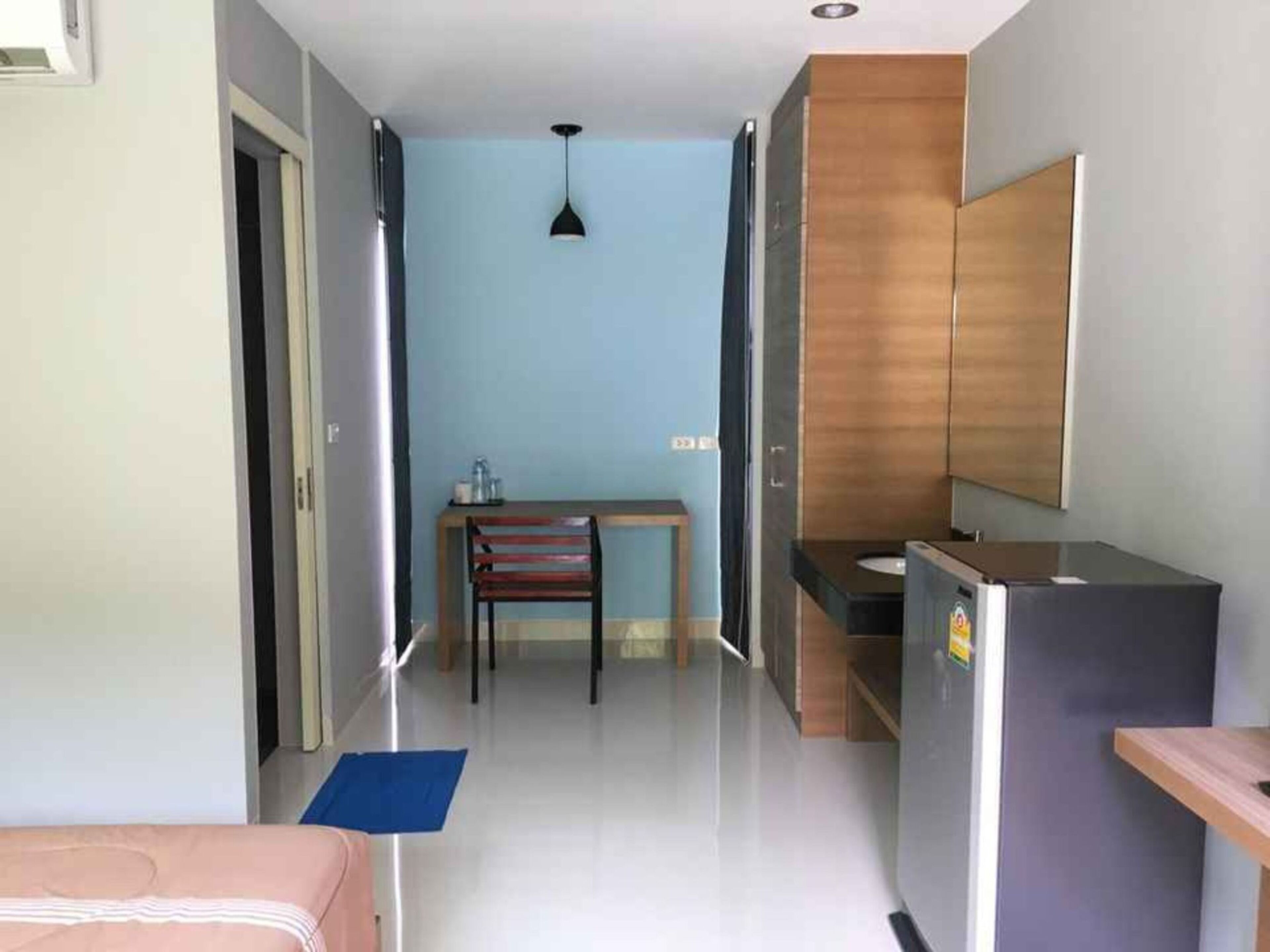 A hotel room with a bed, a desk, a chair, a small table, a refrigerator, and a bathroom with a mirror.