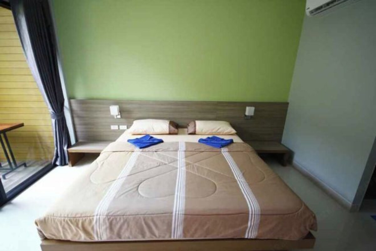 A single bed with a beige and brown bedspread, two pillows, and two folded towels on the bed.