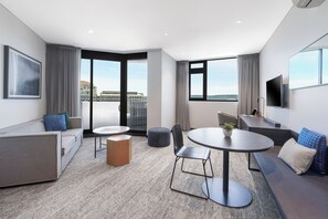 A modern hotel room with a balcony, a sofa, a round table, and a desk with a laptop. - Quest Penrith (Penrith)