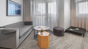 Una sala de estar moderna con un sofá gris, una mesa de centro redonda, un pequeño otomaní y una mesita de noche blanca con una planta.