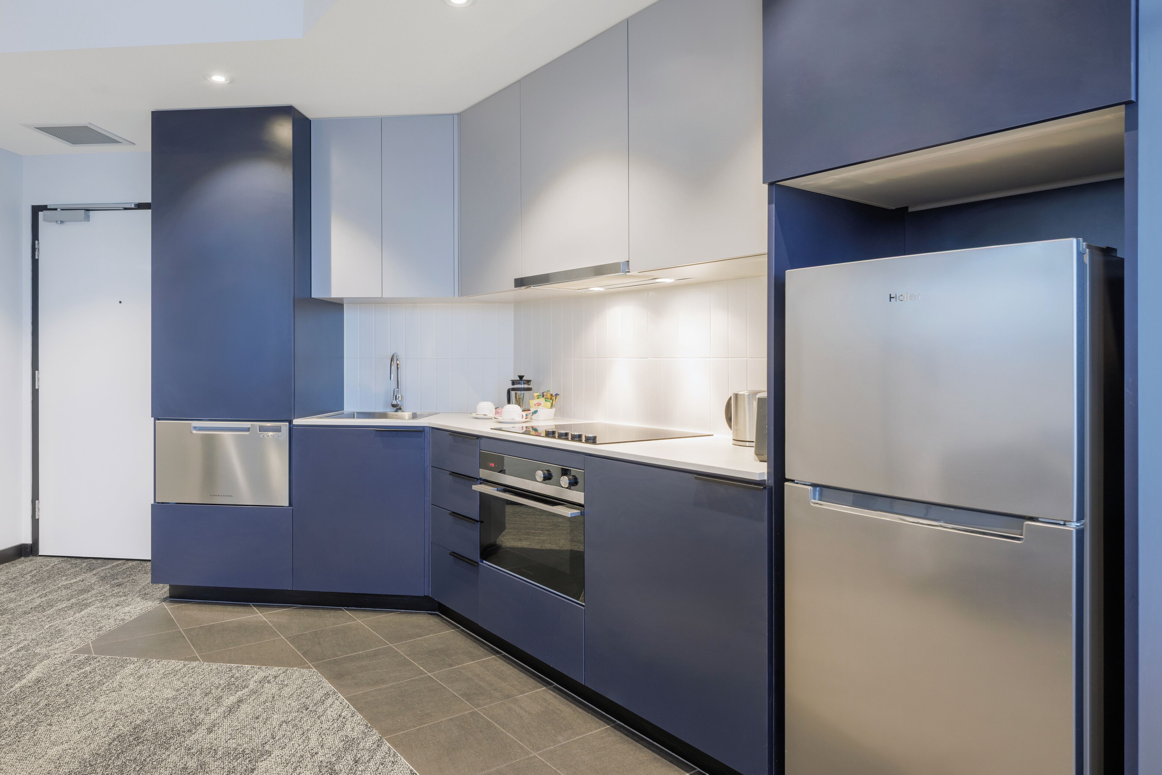A modern kitchen with blue cabinetry, stainless steel appliances, and a tiled backsplash.