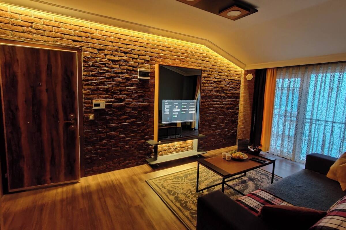 A modern living room with a stone wall, a wooden door, a flat-screen TV, a coffee table, and a sofa.