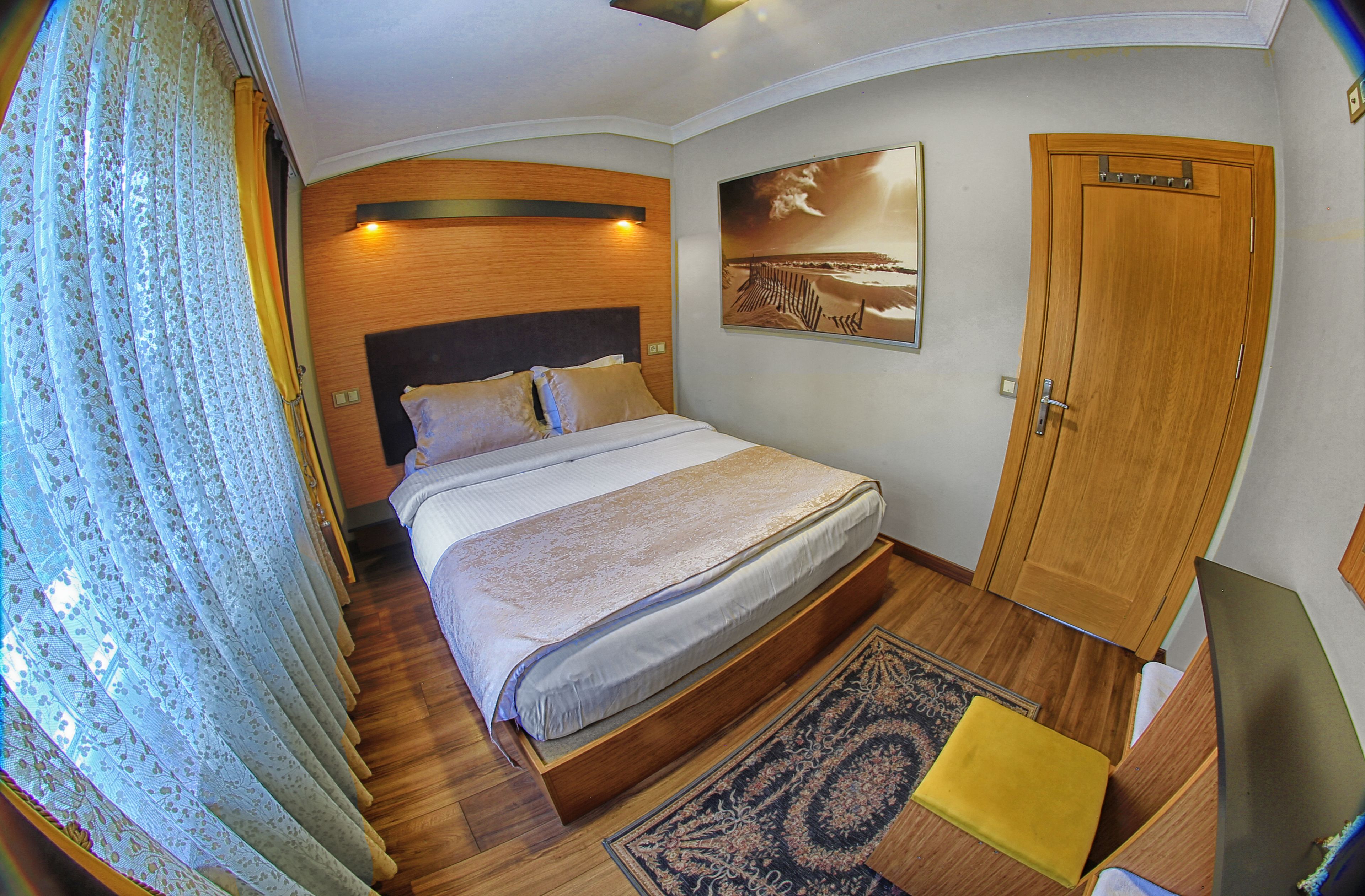 Un dormitorio con cama, cabecero de madera, un cuadro, un armario y una alfombra estampada.