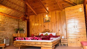 A wooden cabin room with a bed, a stone wall, and a wooden ceiling. - Trinetra Orchards (Dhari)