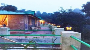 A building with a green roof and a pathway leading to it, surrounded by greenery. - Trinetra Orchards (Dhari)