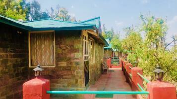 A corridor with stone walls and red railings leading to multiple rooms with green roofs.