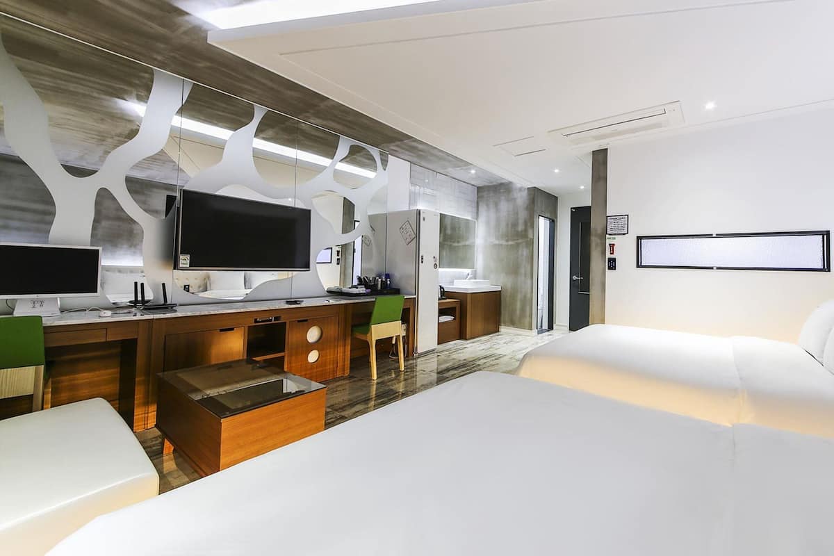 Ein modernes Hotelzimmer mit Flachbildfernseher, Schreibtisch mit Computer, Bett und Badezimmer.
