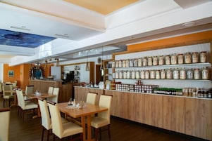 Um restaurante com balcão de madeira, prateleiras com potes e um mural no teto.