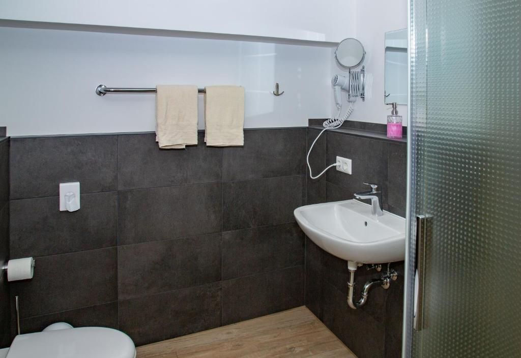 Ein modernes Badezimmer mit Toilette, Waschbecken, Handtuchhalter mit zwei Handtüchern, Föhn und Spiegel.